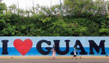 Des touristes passent devant une affiche "I love Guam", sur l'île de Guam dans l'océan pacifique, le