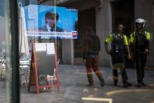 Des policiers catalans marchent devant un bar à Barcelone, dans lequel est diffusé une conférence de