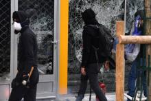 Des manifestants masqués marchent à côté de la vitrine détruite d'un magasin en marge de la manifestation du 1er mai 2018 à Paris