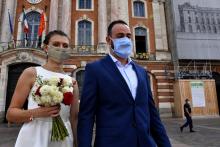 Un couple de mariés pose avec masque devant l'hôtel de ville, sur la place du Capitole à Toulouse, le 21 août 2020